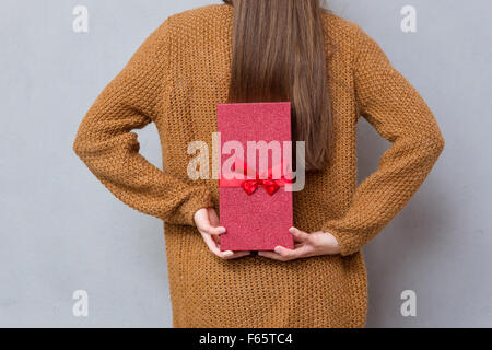Vista posteriore di mani femminili in marrone maglione azienda confezione regalo rossa con nastro Foto Stock