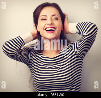 Felice di ridere giovane donna informale con gli occhi chiusi tenendo la testa. Vintage closeup ritratto Foto Stock