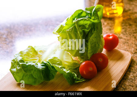 La lattuga, pomodoro e cipolla verde, bambù tagliere e olio sul piano del banco in granito, retroilluminato Foto Stock