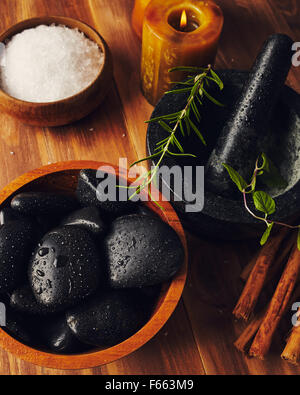 Strumenti spa, sale da bagno, mortaio con erbe aromatiche, una ciotola con pietre calde e candele, alcune stecche di cannella sul tavolo Foto Stock