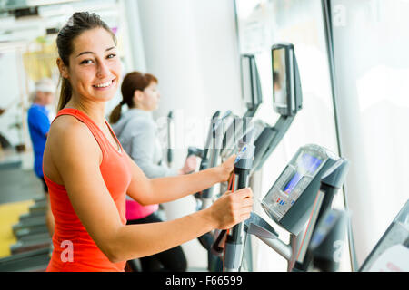 Montare la giovane donna con un trainer ellittico in un centro fitness e sorridente Foto Stock