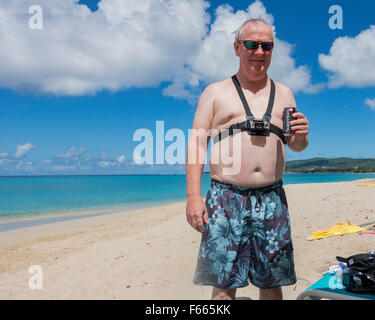 Cinquant'anni di vecchio uomo caucasico con un Go Pro camera legato al suo petto, ha un soft drink sulla spiaggia di St. Croix, U.S.VI. Foto Stock