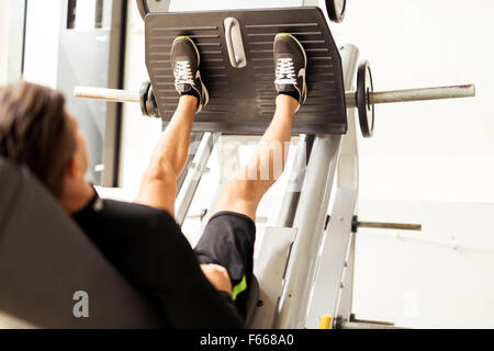 Giovane maschio lavora in una palestra e facendo esercizi di gamba Foto Stock