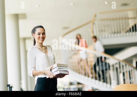 Bella donna contenere libri e sorridente in una biblioteca moderna Foto Stock