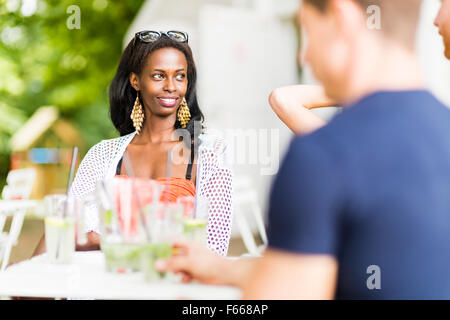 Giovani e felici amici seduti a parlare a un tavolo all'aperto e sorridente Foto Stock