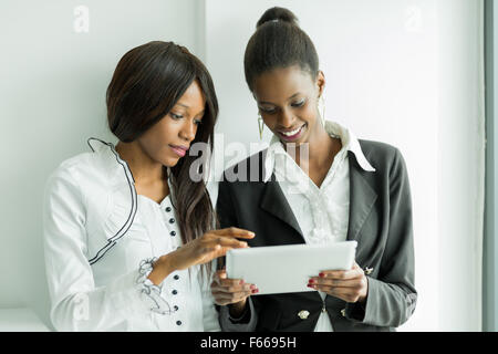 Due colleghi parlare mentre in piedi circa il contenuto su un tablet pc in una ben illuminata ufficio vicino alla finestra Foto Stock