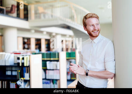 Bello intelligente studente maschio sorridente in biblioteca Foto Stock