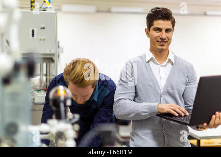 Ritratto di ayoung ingegnere bello di controllare i dati su un computer portatile e sorridente Foto Stock