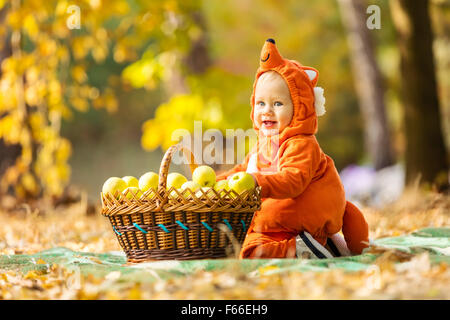 Carino baby boy vestito in costume fox seduta dalla cesta con le mele in autunno park Foto Stock