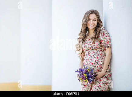 Bella donna incinta con un mazzo di fiori vicino la colonna Foto Stock