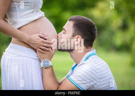 Giovane uomo baciare sua moglie incinta il ventre Foto Stock