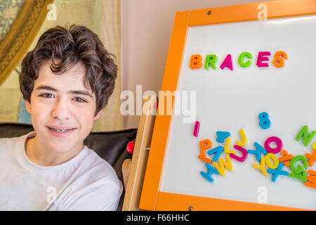 Caucasian ragazzo adolescente attende in sala di attesa nella clinica dentale vicino ad una lavagna dove alcune lettere magnetiche costituiscono la parola bretelle vicino ad altri quelli sfusi Foto Stock