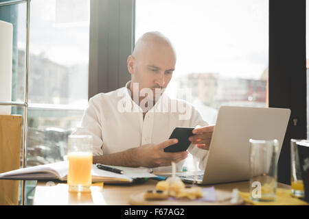 A metà lunghezza dei giovani caucasici bello bald business uomo seduto in un bar usando un computer portatile appoggiato sulle ginocchia, guardando verso il basso lo schermo, pensieroso - lavoro, meditata, concetto di occupato Foto Stock
