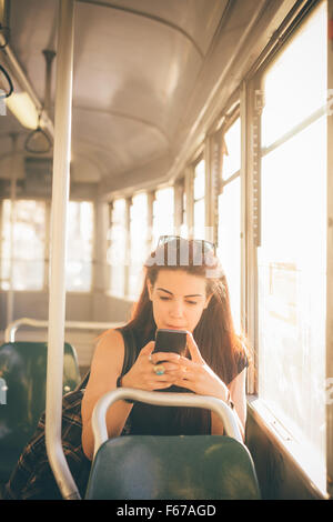 A metà lunghezza di un giovane bella marrone rossiccio capelli donna caucasica utilizzando uno smartphone su un tram - tecnologia, rete sociale, il concetto di comunicazione - guardando verso il basso sullo schermo Foto Stock