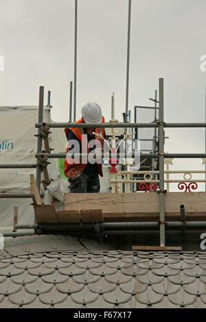 Un pittore prendendo in grande difficoltà per la verniciatura di un Terminale per tenda del tetto sulla parte superiore di stile orientale tetto durante lavori di ristrutturazione. Foto Stock