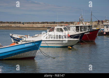 Soleggiata giornata estiva con cielo blu, piccole barche da pesca ormeggiate nel rifugio di frangiflutti e tranquilla, panoramica del porto di mare, Staithes, North Yorkshire, GB, UK. Foto Stock