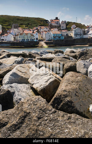 Sunny summer view del pittoresco villaggio di Staithes, North Yorkshire, Regno Unito, visto da dietro le difese del mare (rock corazza barriera) proteggere il porto. Foto Stock