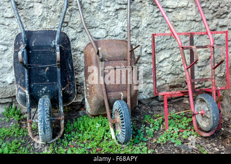 Tre carriole da giardino appoggiate al muro Giardino delle carriole Foto Stock