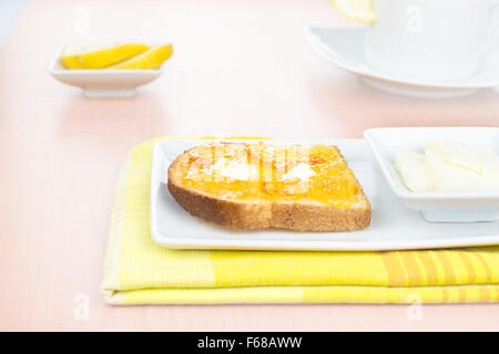 La prima colazione. Toast alla francese con diffusione di arancia amara marmellata o confettura con frutta candita, riccioli di burro, limone, una tazza e stoviglie su Foto Stock