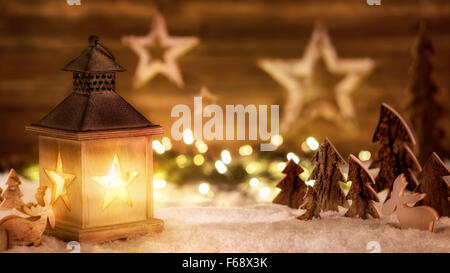 Accogliente disposizione di Natale con bellissimi ornamenti di legno sulla neve nel caldo lume di candela di una bella lanterna, basso-chiave studio sho Foto Stock