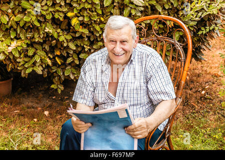 Tranquilla pensione, vecchio uomo legge il giornale in giardino Foto Stock