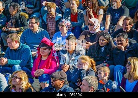 Un ampio e diversificato gruppo di persone al di fuori seduta in righe come un pubblico la visione di una performance live e rispondere gioiosamente Foto Stock