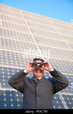 Imprenditore cerca attraverso il binocolo di fronte a pannelli solari Foto Stock