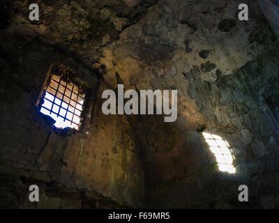 Ha rovinato il carcere prigione di un castello medievale. La luce del sole entra da una finestra con ironia barre arrugginite Foto Stock