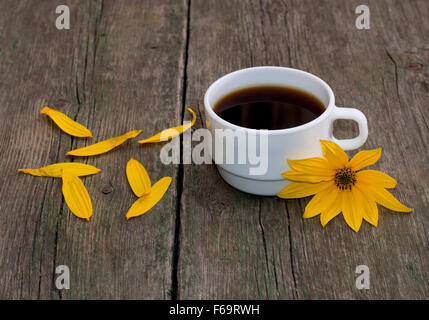 Ancora in vita un bianco tazza di caffè, un fiore giallo e petali, su di un tavolo di legno Foto Stock