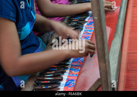 Le mani di una donna di tessitura utilizzando navette con bobine di filo su di un telaio di tessitura. Parzialmente tessuto tessuto di seta visibile. Mandalay, Myanmar. Foto Stock