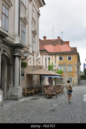 La donna a piedi lungo Lubiana strada stretta di fronte street cafe. La Slovenia. Foto Stock