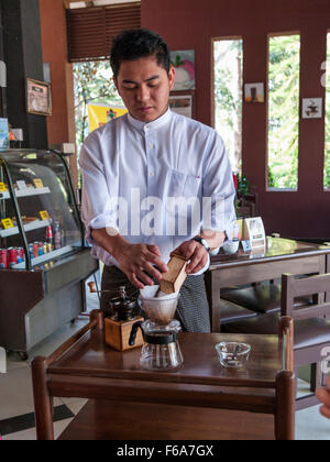 Cameriere in un caffè di Pyin Oo Lwin (Maymyo) in Myanmar la preparazione del caffè fresco, versando la massa i fagioli in un filtro. Foto Stock