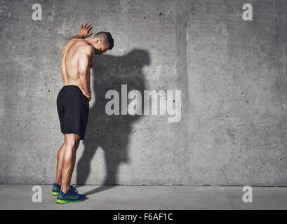 Giovane uomo riposo dopo un attivo allenamento di fitness mentre in piedi contro il muro grigio con Copia area di spazio per il tuo messaggio di testo, Foto Stock