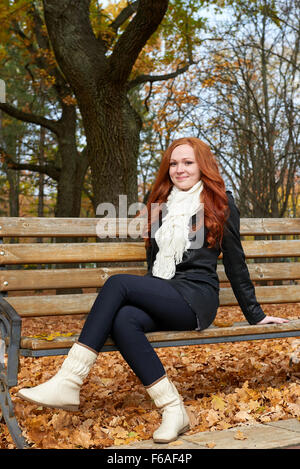 Redhead ragazza seduta su una panchina nel parco cittadino, stagione autunnale Foto Stock