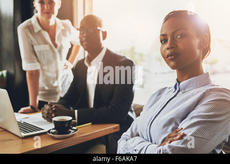 Fiducioso giovane nero business donna seduta davanti ad altre persone di affari Foto Stock