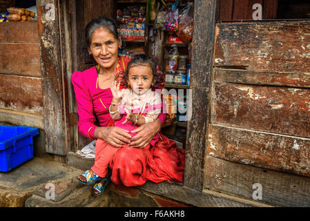 Vecchia Signora nepalese con un bambino vende merci nel suo negozio. Foto Stock