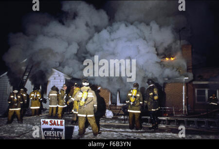 Lanham, Maryland. Stati Uniti d'America, 1980 Prince George County Maryland volunteer fire fighters provare a spegnere un testardo arson incendio in una casa che era in vendita. Il fuoco può essere visto a partire da flash su e soffiare fuori la porta del seminterrato formando un diavolo di fuoco. Credito: Mark Reinstein Foto Stock