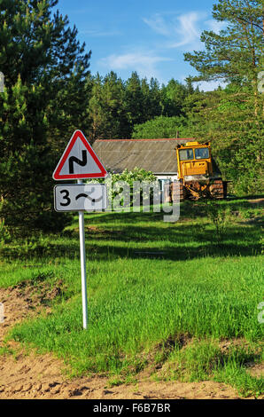 Strada di foresta.il cartello stradale indica che la strada di ritorcitura. Vicino alla strada i bulldozer. Foto Stock