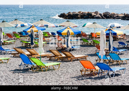 Santorini, Thira. Kamari beach con vuoto sun poltrone reclinabili disposte in coppie e ombrelloni, alcuni chiuso, alcuni aperti. Il mare e il cielo dello sfondo. Foto Stock