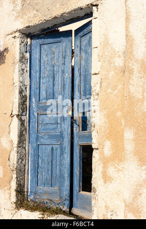 Le Cicladi, Santorini. Muro di casa, il rendering di gesso patchato e riparata, semplice doppia porta con mezza aperta weathered vernice scrostata blue porta di legno. Foto Stock