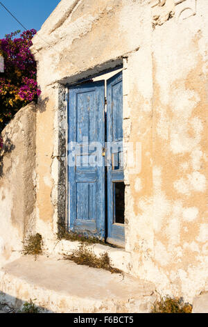 Le Cicladi, Santorini. Muro di casa, il rendering di gesso patchato e riparata, semplice doppia porta con mezza aperta weathered vernice scrostata blue porta di legno. Foto Stock