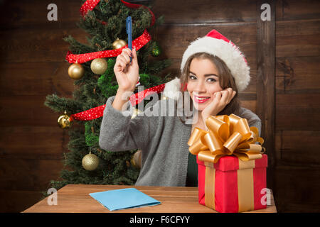 Ritratto di bella ragazza seduta al tavolo di legno e pensare a nuove e interessanti Anno e Natale COMPLIMENTI A Foto Stock