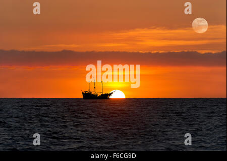 Nave silhouette tramonto è un vecchio legno nave pirata seduti al mare con la luna piena che sorge nel Cielo di tramonto. Foto Stock