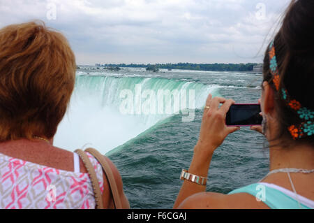 Una donna scatta una fotografia con un telefono del ferro di cavallo cade dalla parte superiore del lato canadese delle Cascate del Niagara. Foto Stock