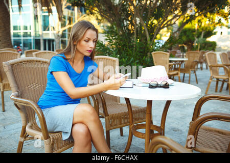 Candida immagine di un giovane piuttosto moderno blogger utilizza lo smartphone e prende appunti in un notebook in un cafe Foto Stock