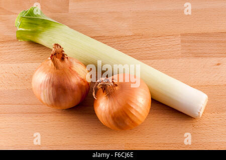 Due cipolle fresche e un porro su una tavola di legno di sfondo, Foto Stock