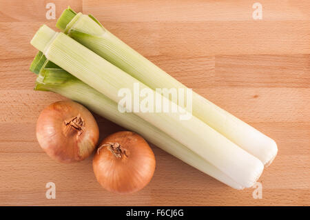 Due cipolle e tre porri su una tavola di legno. Foto Stock