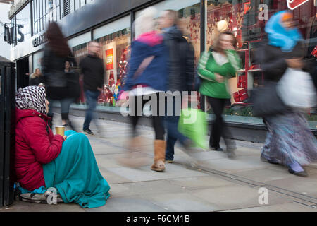 Persone che passano Senzatetto femmina dell'Europa orientale Beggar seduto sul marciapiede fuori dal negozio Debenhams, Piccadilly. Homelessness a Manchester, Regno Unito Foto Stock