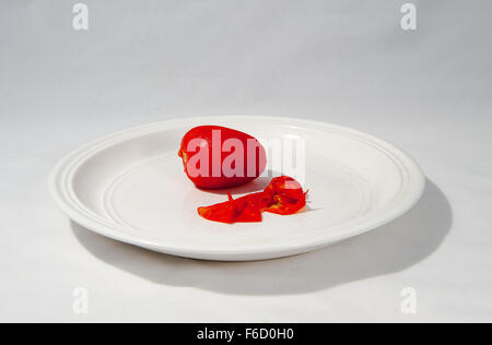 Un pelato di pomodoro rosso e la pelle su una piastra bianca Foto Stock