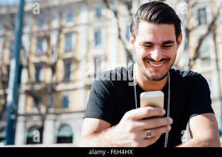 Ritratto di un giovane bello ragazzo italiano utilizzando uno smartphone connesso online, guardando verso il basso lo schermo, sorridenti - tecnologia, sociale un concetto di rete Foto Stock